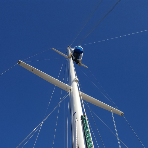 Man on mast installing new sail rigging